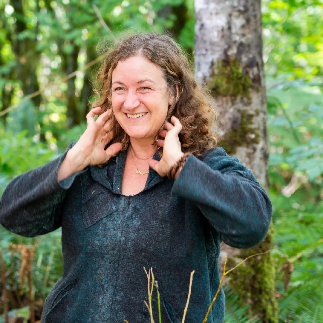 Smiling woman with curly hair standing among trees and ferns in a green forest