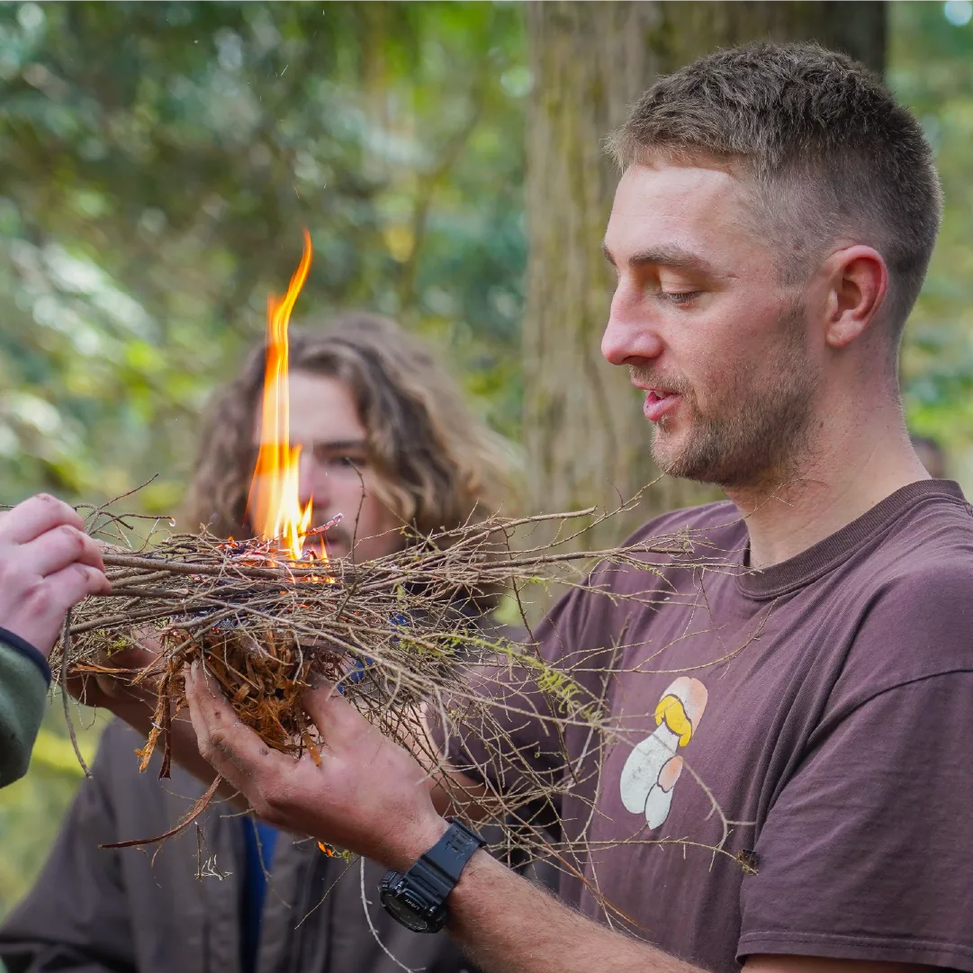 Instructor holding a bundle of twigs as it bursts into flame during a friction fire lesson