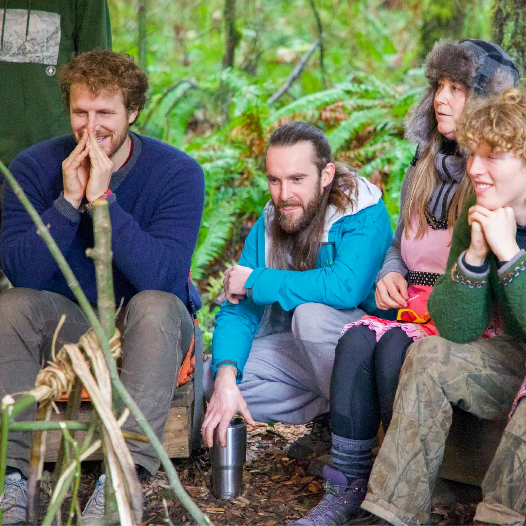 Group of students sitting together on the forest floor, smiling and talking