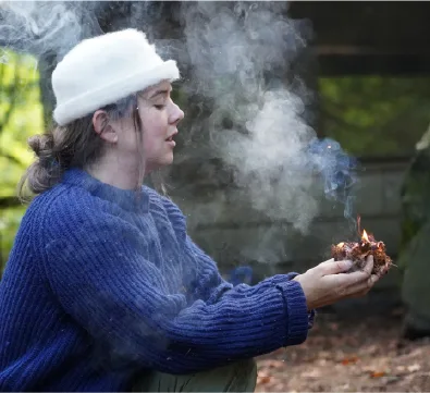 Student in a white beanie tending a smoky fire